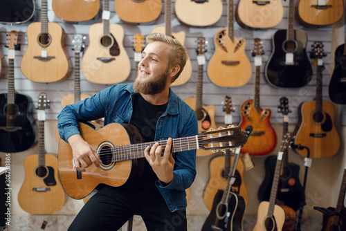 Young man plays on acoustic guitar in music store