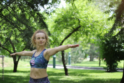 Girl with curly blond hair doing yoga outdoors in the park.
