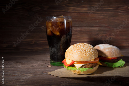 Two BBQ hamburgers with cola on wooden background.