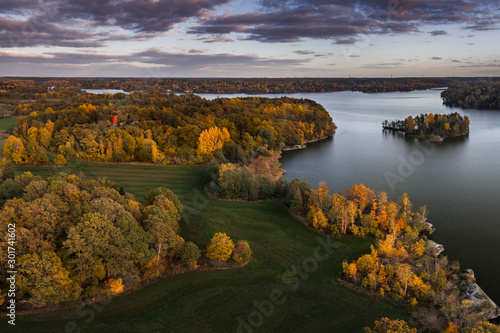 Aerial view of orange and yellow autumn trees and green fields around a lake