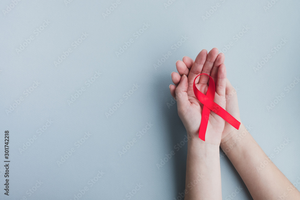 Womans hands hold red ribbon awareness Aids on a light blue background. Medicine concept, World Aids day campaign. Top view, copy space - obrazy, fototapety, plakaty 