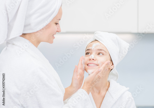Smiling mom washes face her daudther in bathroom at home