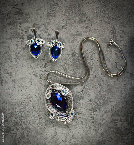 Luxurious and elegant soutache jewelry set, on silver and sapphire colour. Hand sewned jewels on grey background.