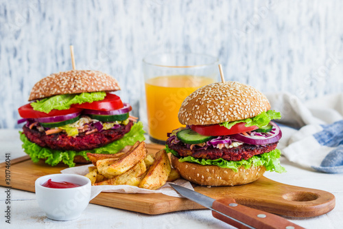 healthy vegan burger with beet cutlet coleslaw salad fresh vegetables fries potato and bowl with sauce glass of orange  juice