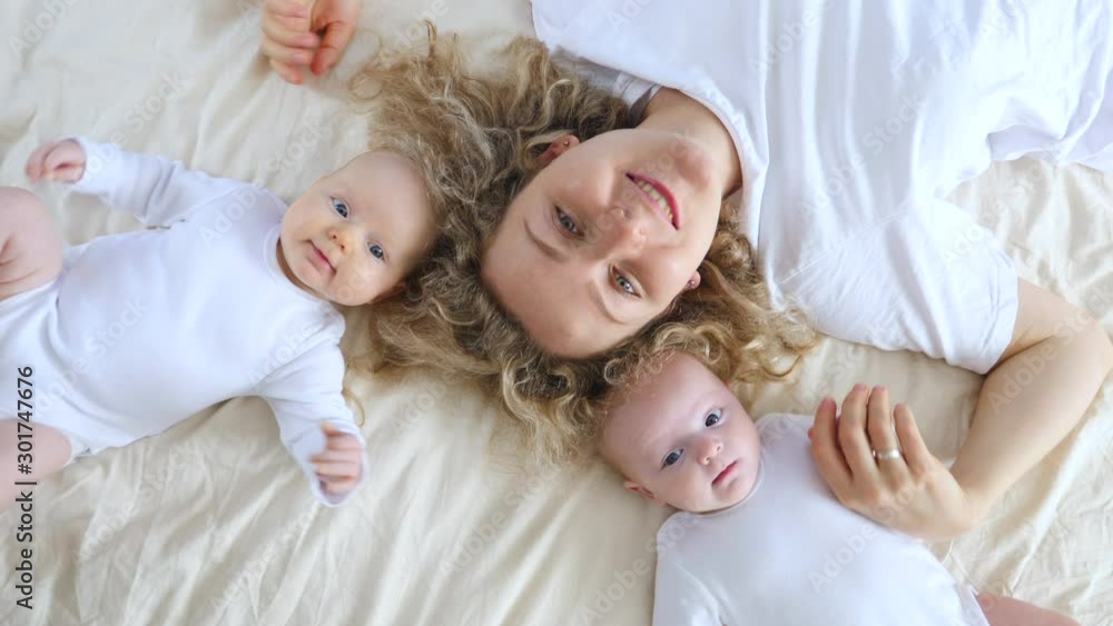 Happy Mother Lying On Bed With Her Two Baby Girls.