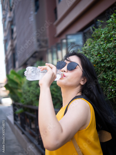 Asian tourist woman drinking a bottle of water in Hua Hin city, travel concept.