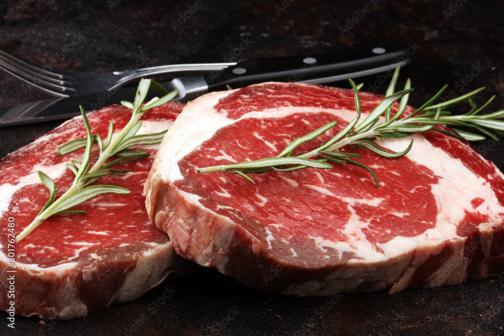 Raw fresh meat Ribeye Steak, seasoning and meat fork on rustic background