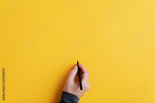Male hand writing on a blank yellow surface with black marker photo