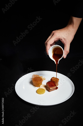Slika na platnu Hand pouring sauce over food on a plate, exquisite dish, creative restaurant meal concept