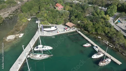 Aerial shot of a small marina in Boka-Kotor bay, Montenegro, with moored boats and yachts, on a sunny summer day. The water in the sea is emerald, mountains are visible in the background photo