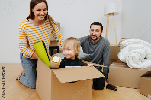 Happy young family moving to a new home, unpacking cardboard boxes with joy
