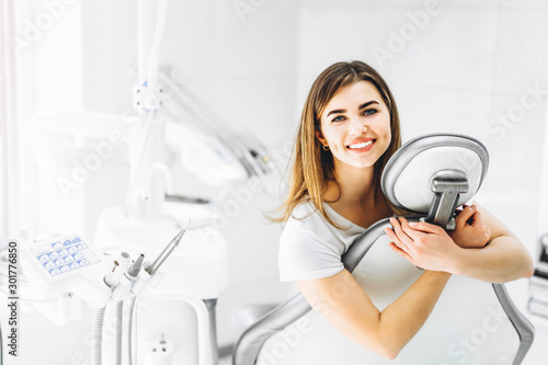 Portrait of a happy young patient after the dental examination. A woman sitting hugging armchair in withe modern dentist office