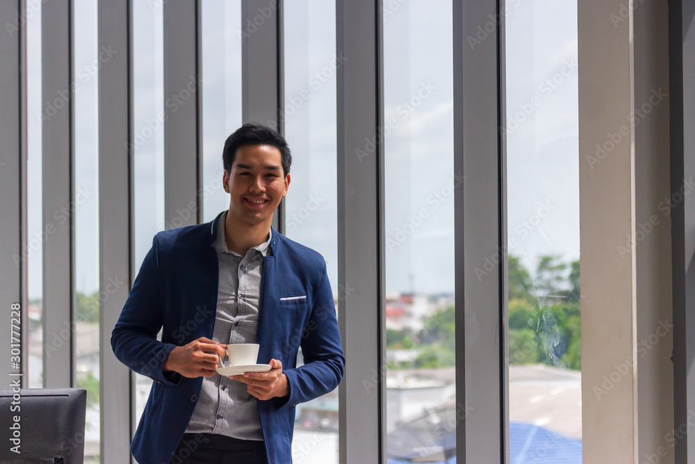Fototapeta premium A young Asian businessman drinks coffee in the office window in a comfortable
