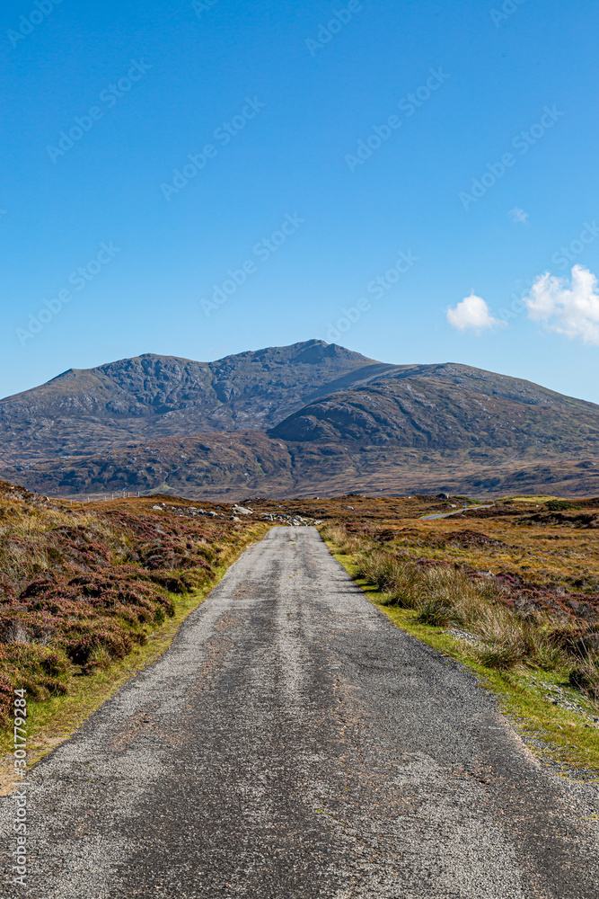 A long single track road on the Hebridean island of South Uist with mountains in the distance