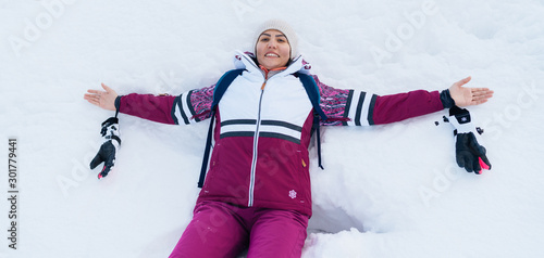 Young smiling female liying on the white snow wide opened her arms. photo