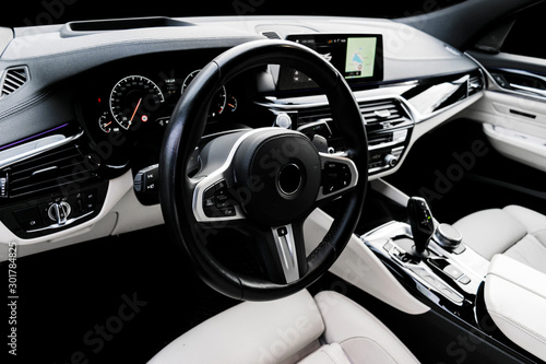 Modern luxury car white leather interior with natural wood panel. Part of leather car seat details with stitching. Interior with dashboard. White perforated leather. Car detailing. Car inside