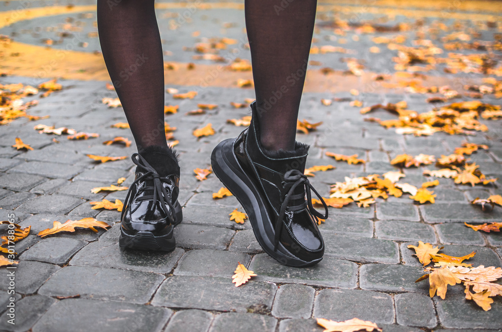 A girl walks in black shiny warm shoes on a tile with leaves in the city center in a park A girl walks in black shiny warm shoes on a tile with leaves in the city center in a park