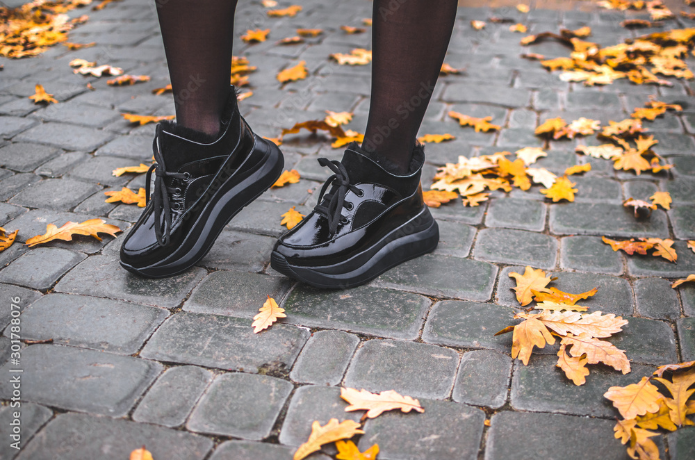 A girl walks in black shiny warm shoes on a tile with leaves in the city center in a park A girl walks in black shiny warm shoes on a tile with leaves in the city center in a park