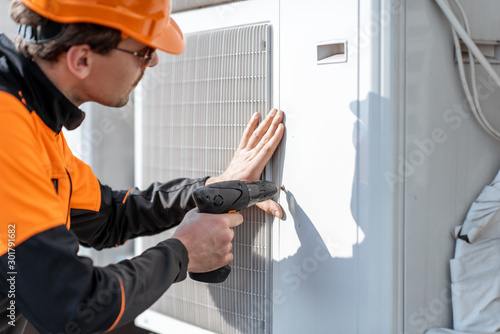 Professional workman in protective clothing installing or reparing outdoor unit of the air conditioner or heat pump on the rooftop photo