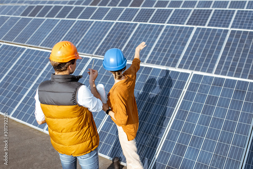 Two engineers or architects examining the construction of a solar power plant, standing with digital tablet between rows of solar panels