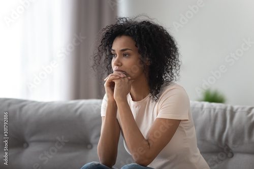 Upset African American woman thinking about problem at home alone photo