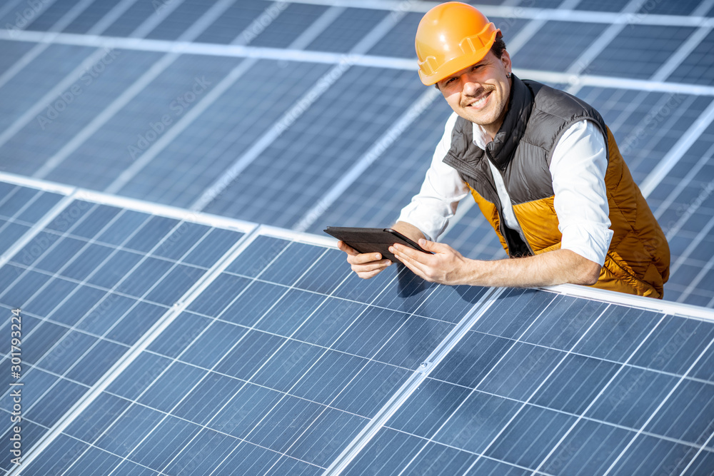 Portrait of a happy engineer in protective helmet standing with digital tablet on a solar power plant. Solar station development concept Portrait of a happy engineer in protective helmet standing with digital tablet on a solar power plant. Solar station development concept