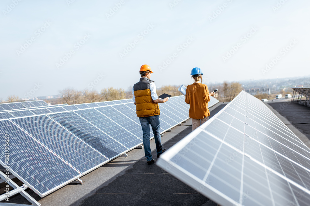custom made wallpaper toronto digitalView on the rooftop solar power plant with two engineers walking and examining photovoltaic panels. Concept of alternative energy and its service