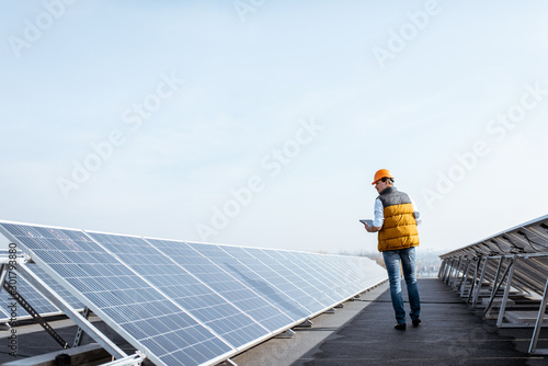 View on the rooftop solar power plant with mann walking and examining photovoltaic panels. Concept of alternative energy and its service photo