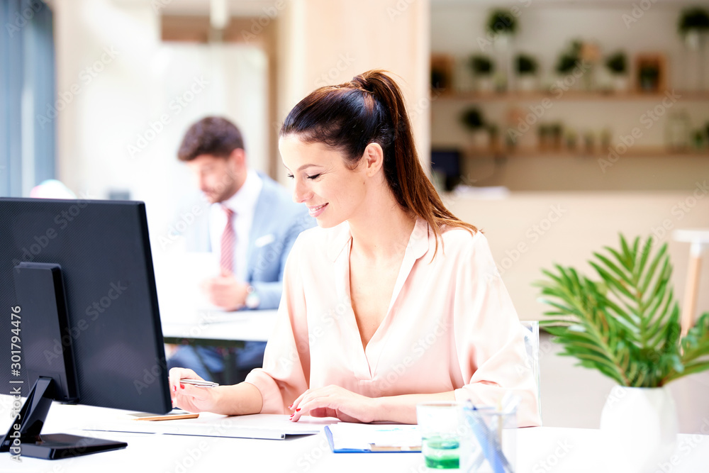 Beautiful businesswoman sitting at office desk and working on computer Beautiful businesswoman sitting at office desk and working on computer