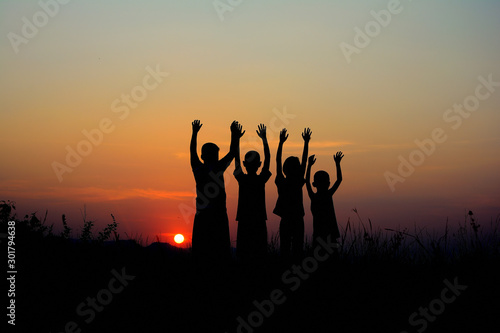 Black silhouette of four children standing together. There is a sky at sunset background