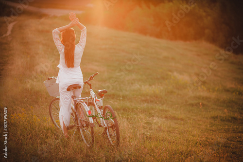 beautiful young woman on a bicycle in a white dress in the evening