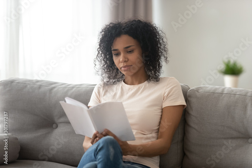 Focused serious African American woman reading book at home