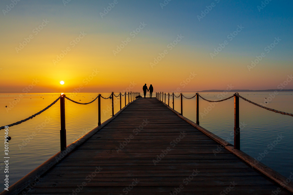 couple in love meets the dawn on the pier. sunrise over the water. Silhouettes of man and woman. romantic morning