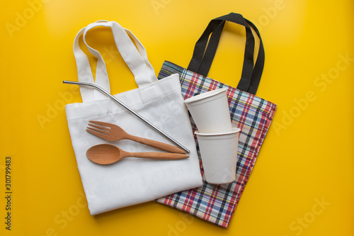 Flat lay of sustainable products, spoon wooden and stainless straw in cloth bag on yellow background, environment and eco concept.