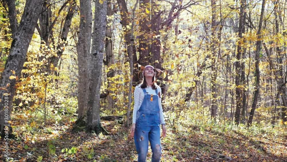 Happy young woman having fun, laughing and throwing yellow leaves at autumn forest in sunny day. Leaves is falling in slow motion. Happy young woman having fun, laughing and throwing yellow leaves at autumn forest in sunny day. Leaves is falling in slow motion.