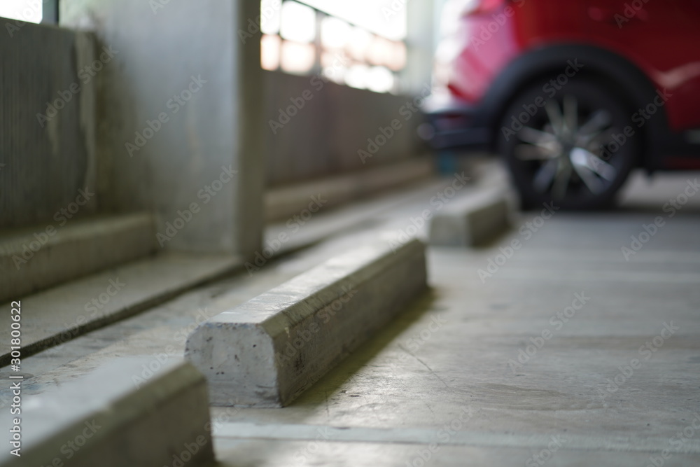 Car parking lots at business tower are available. Close up and selective focus at the parking stopper object. There is a red car parked as background.