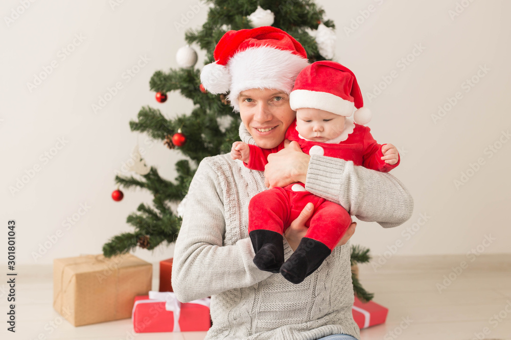 Father with his baby boy wearing Santa hats celebrating Christmas.