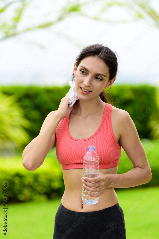 Fototapeta premium Beautiful woman runner has tired and rest for drinking water and a white towel to wipe her face after running in the garden.