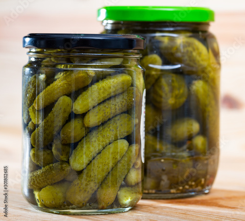 Glass jar with pickled cucumbers on wooden background
