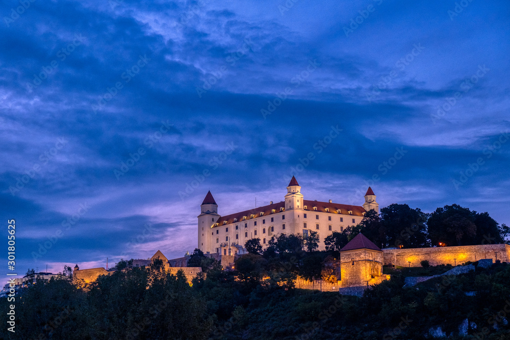 Bratislava castle illuminated in evening glow against dramatic sky