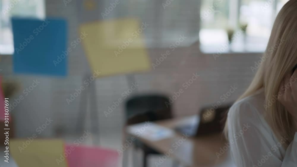 portrait of a successful girl medium shot, serious stressful stressful business woman talking on the phone and taking notes on stickers. modern office with glass wall 4K portrait of a successful girl medium shot, serious stressful stressful business woman talking on the phone and taking notes on stickers. modern office with glass wall 4K