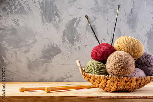 Skeins of yarn for knitting from natural wool in a wicker basket. Wooden surface or table. Background - concrete wall. Wooden knitting needles.