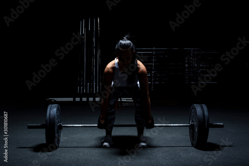 Anonymous woman bodybuilder make workout - weight lifting with barbell. Light from above, dark background.