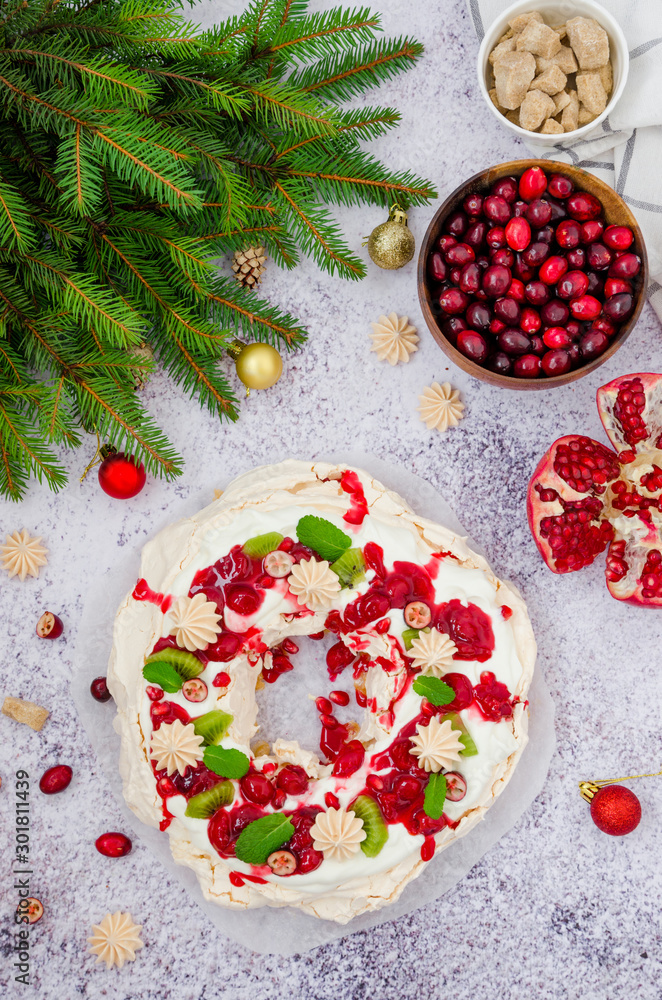 Caramel Pavlova Christmas wreath with cherry sauce, pomegranate, cranberries and kiwi on a light stone background. Festive dessert for Christmas and New Year. Caramel Pavlova Christmas wreath with cherry sauce, pomegranate, cranberries and kiwi on a light stone background. Festive dessert for Christmas and New Year.