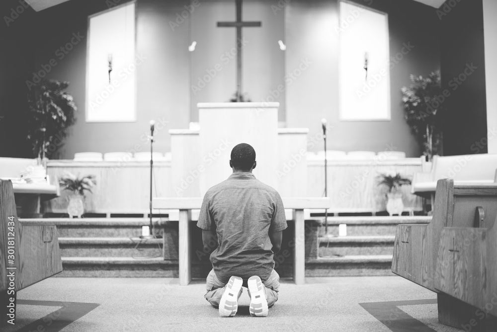 Grayscale of a male on his knees praying in the church with a blurred background - obrazy, fototapety, plakaty 