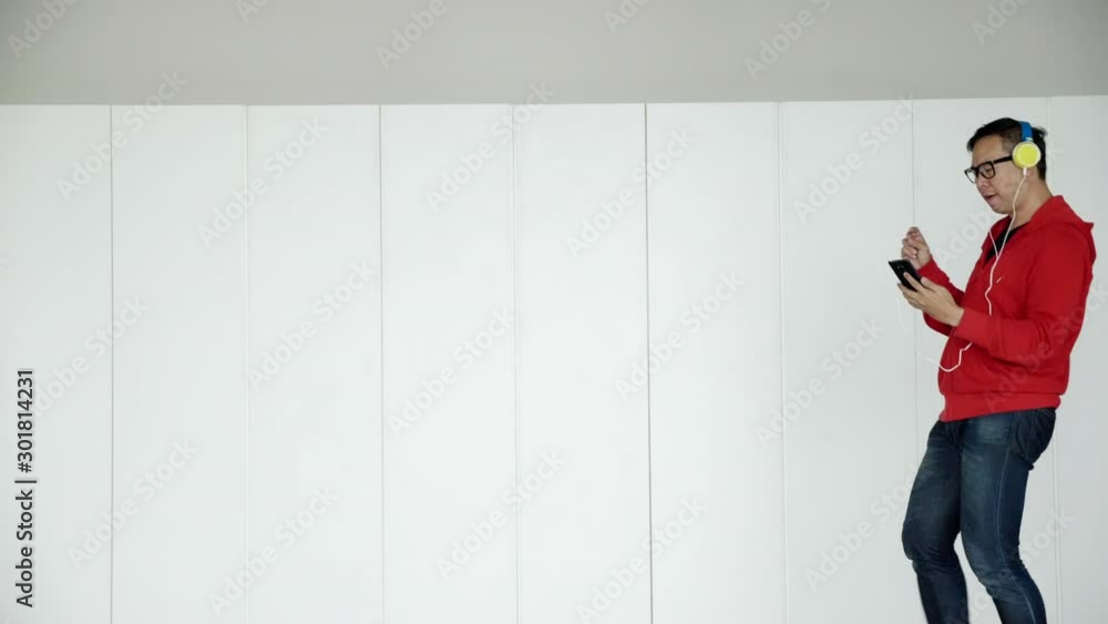 4K Slow motion: Freelance Asian men wear black glasses, red shirts wear headphones Walking, listening to music on smartphone and dancing happily in the office. Successful work with happy emotions