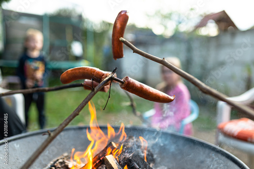 Sausages on a wooden stick baked over a bonfire in the home garden.