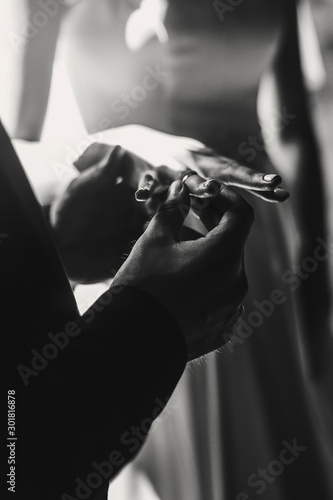 Wedding couple exchanging wedding rings during holy matrimony in church. Bride and groom putting golden rings on finger, close up. Spiritual moment. Black and white