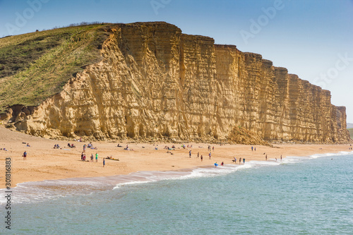 Φωτογραφία People relaxing and sunbathing on Bridport beach with dramatic layered cliffs of