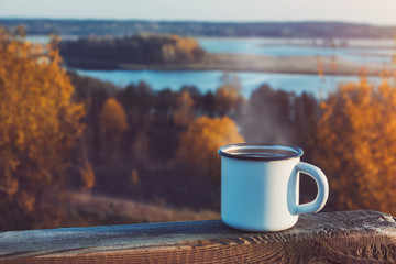 Enameled cup of coffee or tea on autumn landscape outdoors.